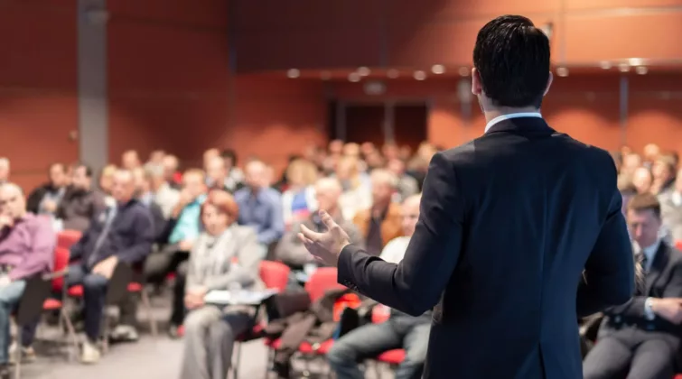 Homme de dos donnant une conférence face à un public de professionnels