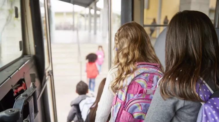 Des enfants avec des sacs sur le dos descendent du bus scolaire