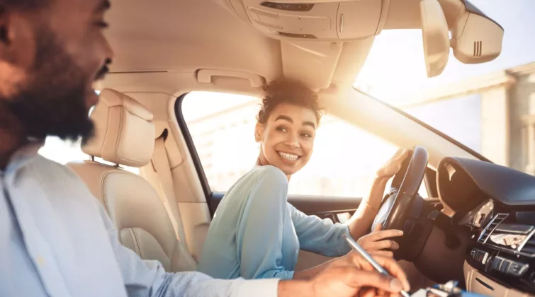 Une jeune femme assise au volant d'une voiture pour passer son permis sourit à son examinateur