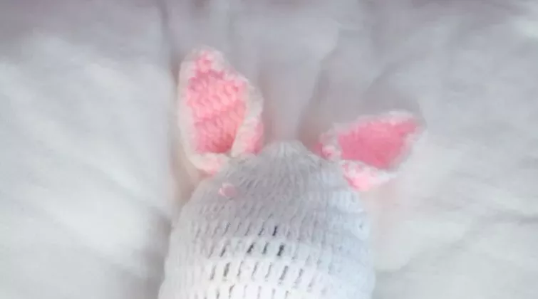 bébé en bonnet allongé sur du textile blanc