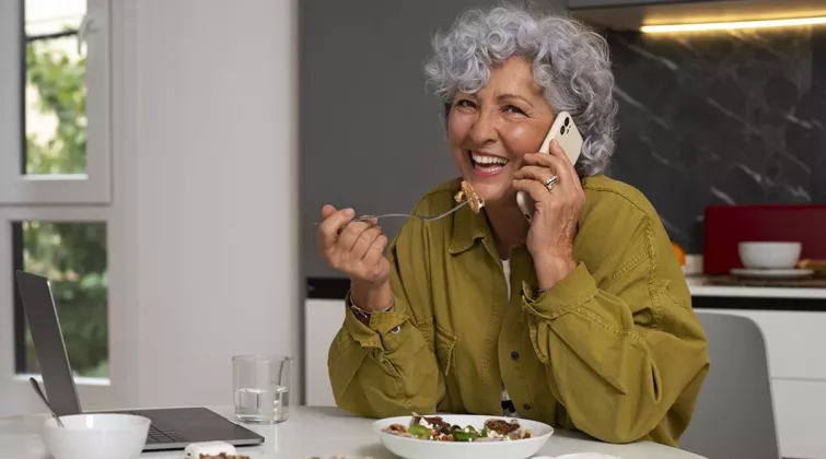 Une femme senior mange une salade tout en répondant au téléphone