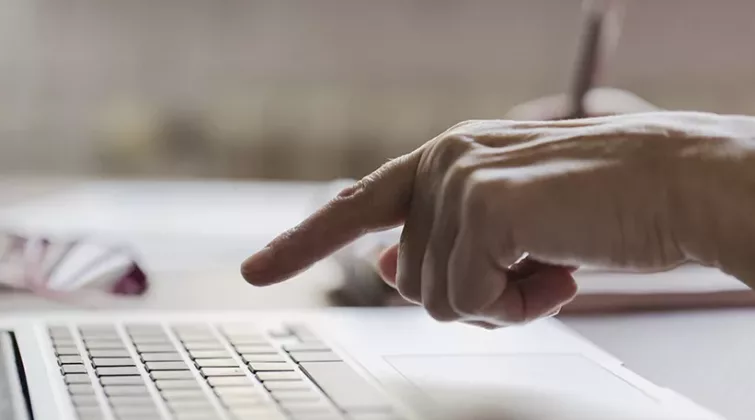 une main de personne âgée au-dessus d'un clavier de portable