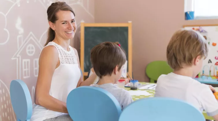 une femme souriante regarde l'objectif, assise à une table colorée à côté de deux jeunes enfants