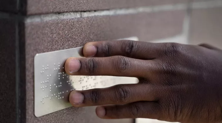la main d'une personne noire posée sur une plaque métallique en braille - crédit photo : freepik